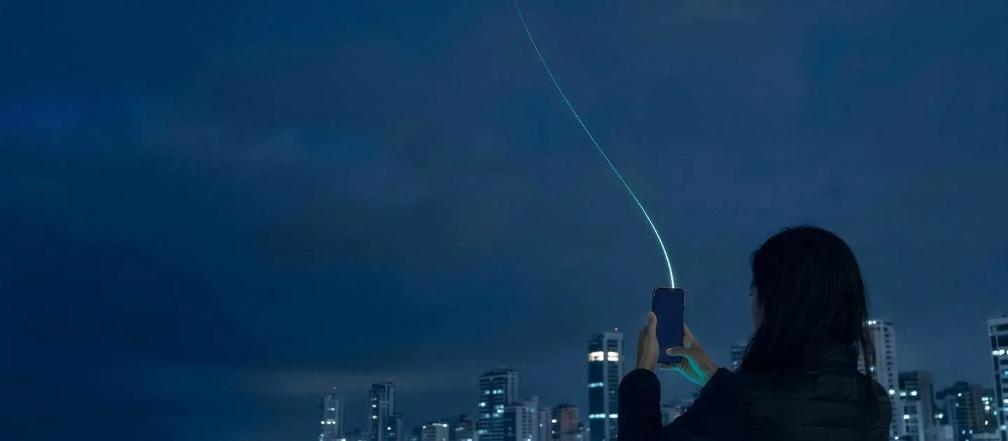 Persona en una azotea frente a la ciudad de noche; un hilo de luz une su teléfono con el cielo