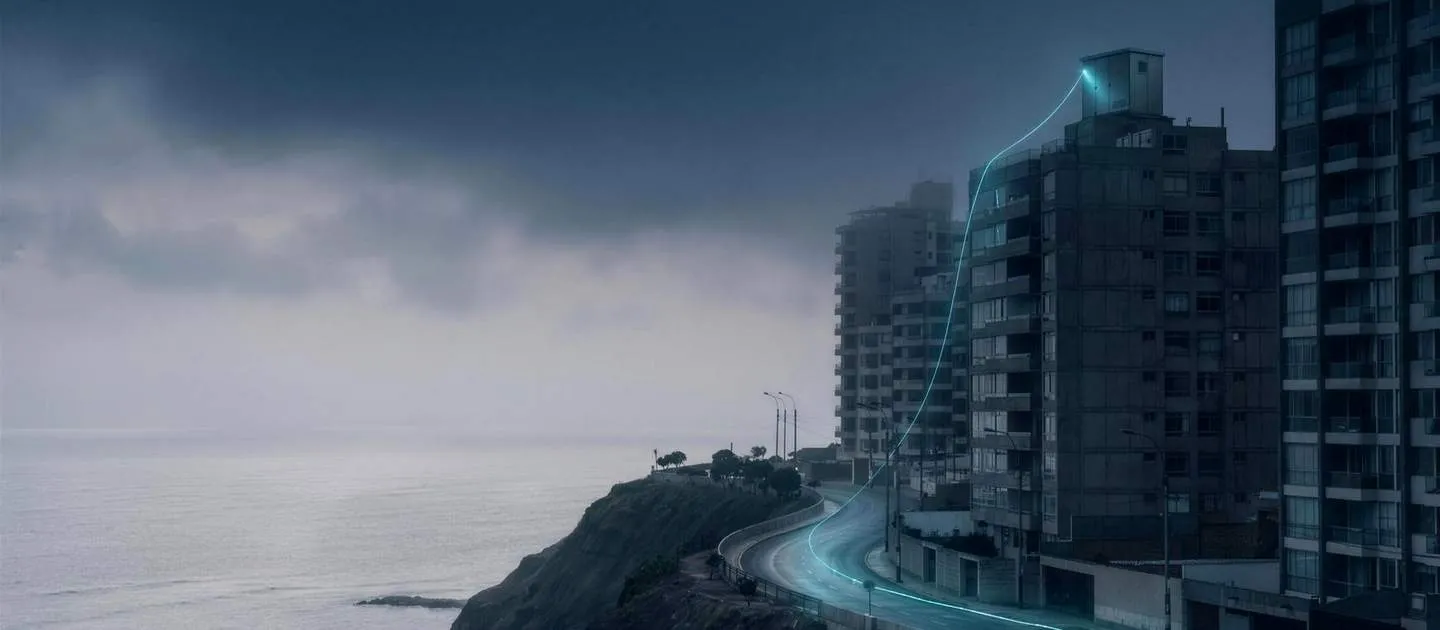 Edificios frente al mar bajo un cielo nublado; un trazo de luz recorre la costa
